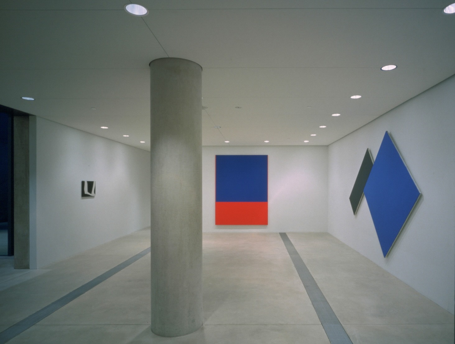A view of Kelly's work in the Entrance Gallery, which includes a large blue and black painting, a large blue and orange painting, and a small black and white painting.