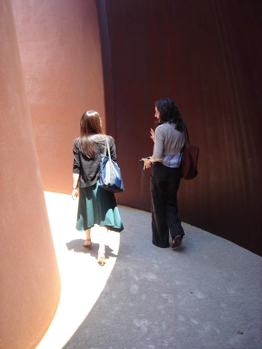 Two visitors chat and walk through Serra's "Joe," its walls casting a shadow between them.