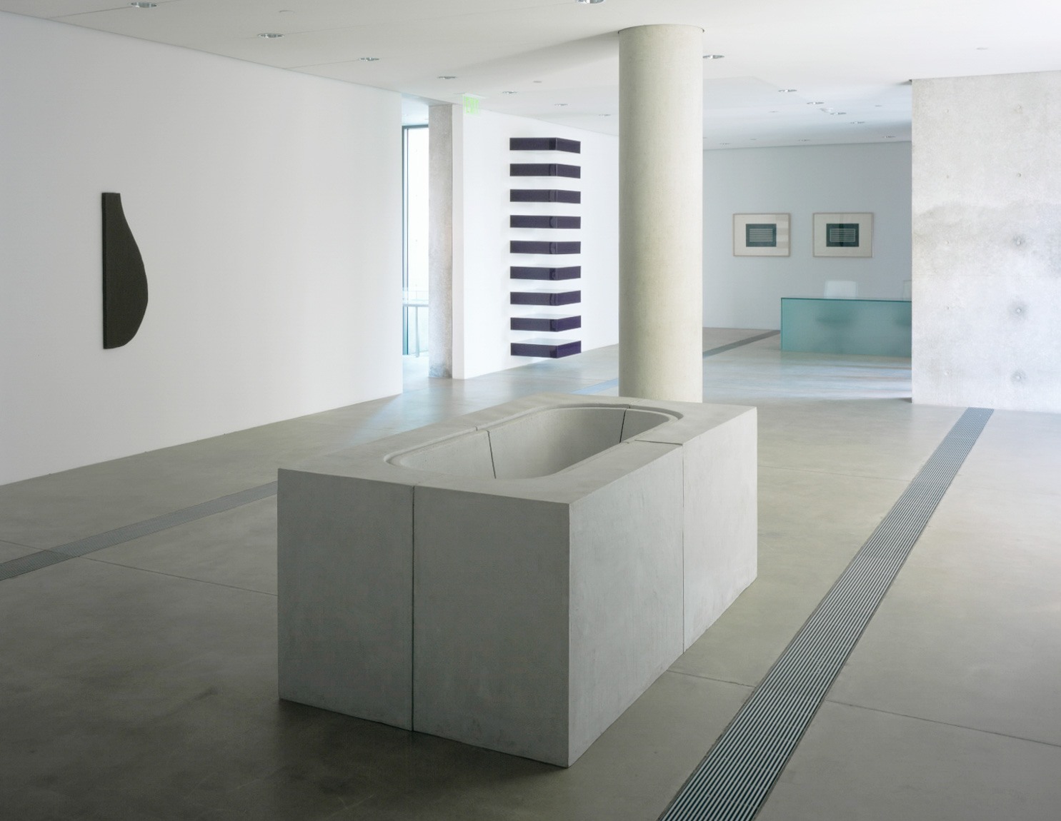 A concrete tub sits on the concrete floor of the Entrance Gallery, with a stack by Donald Judd behind it, and a black Kelly painting on the wall across from it.
