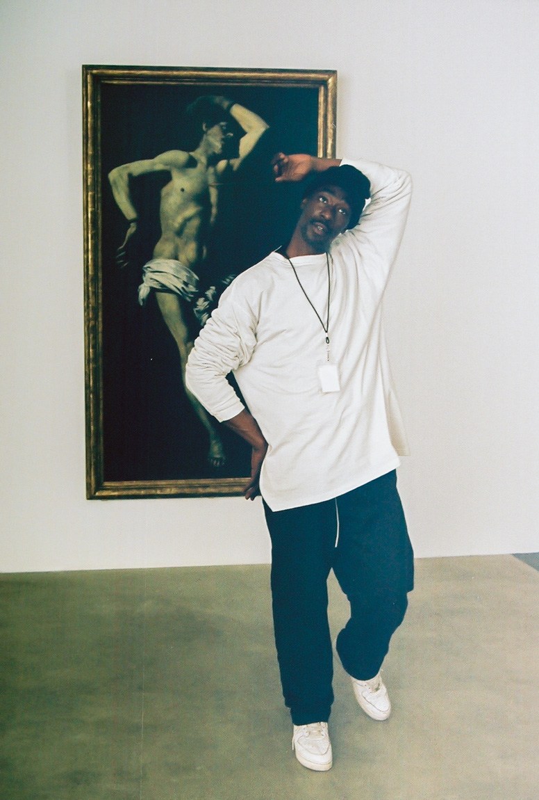 A performer poses to replicate a figure in a painting behind them.