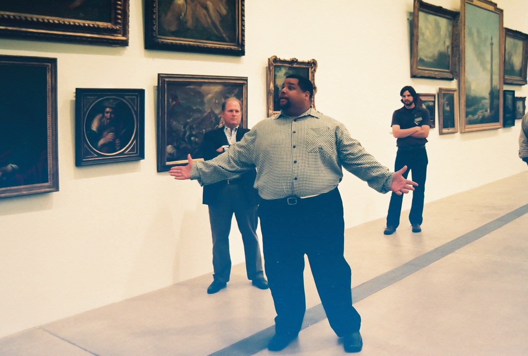 An individual speaks to a crowd in front of a wall of paintings in the Main Gallery.