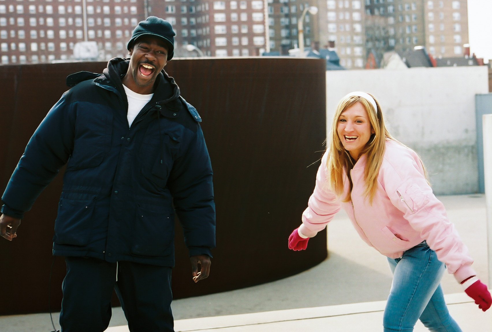 Two participants wearing winter clothes laugh together in the Courtyard in front of "Joe" by Richard Serra.