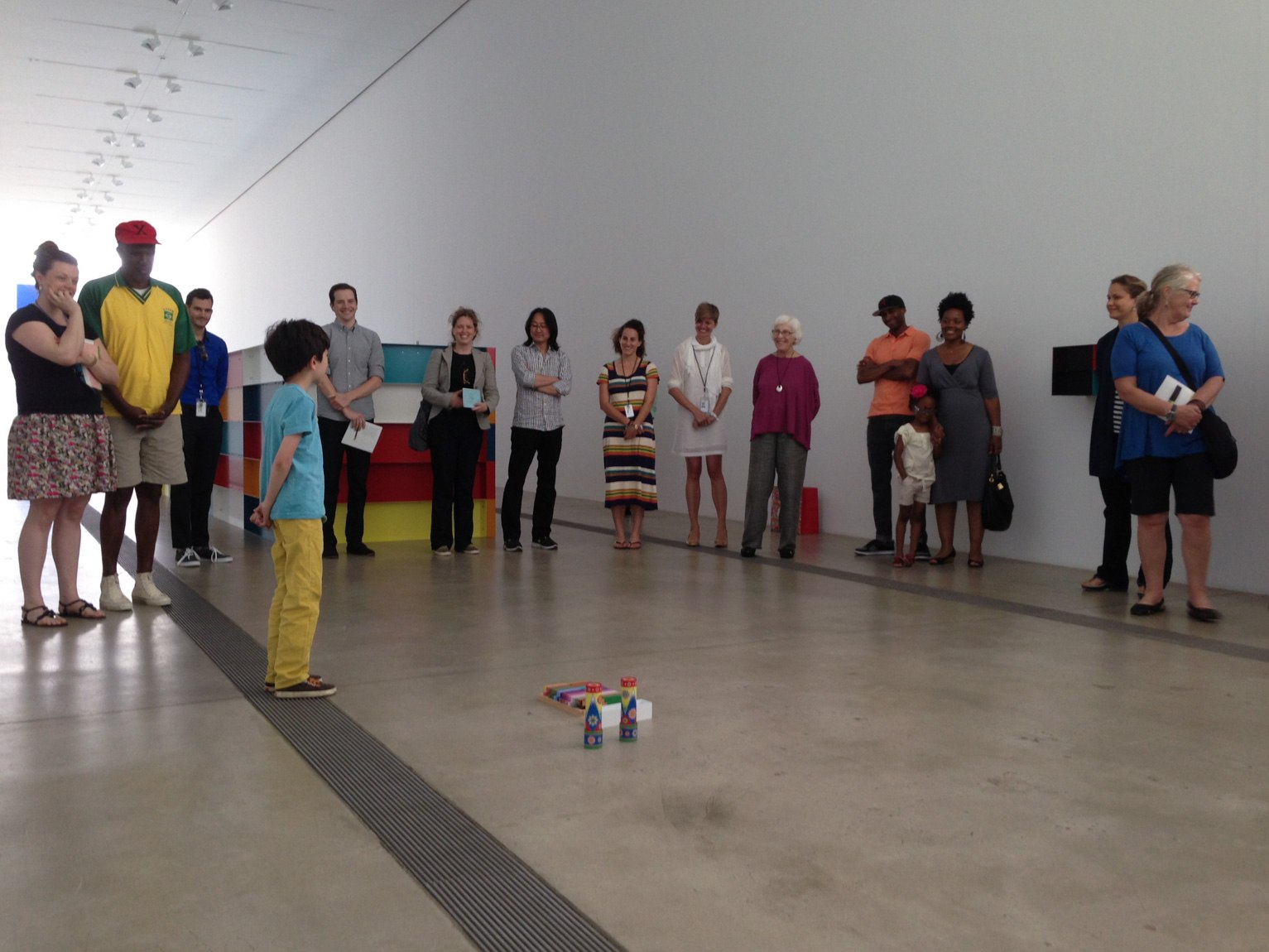 Participants gather in a large circle in the Main Gallery around a child talking to them. A colorful toy sits on the ground beside them.