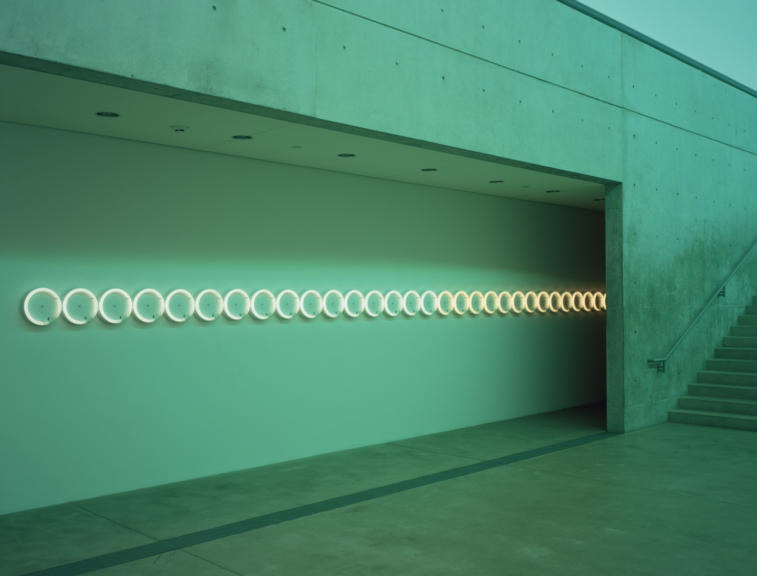Flavin's "untitled (in memory of Barbara Schiller)," a row of fluorescent white circles, is installed along the Lower Corridor in the glow cast by Flavin's "untitled (to my dear bitch, Airily)."