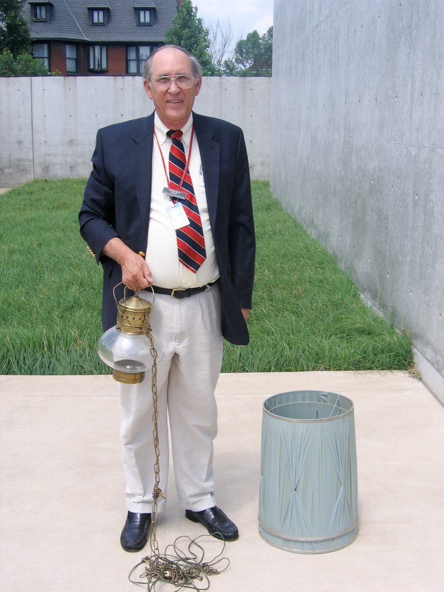 A Lamp Project donor holds a pendant lamp and tall lampshade sit on the ground beside them.