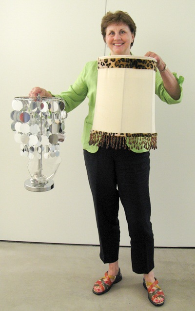 A Lamp Project donor smiles with their lamps, one an animal print lamp with tassels, the other a metallic disc silver lamp.