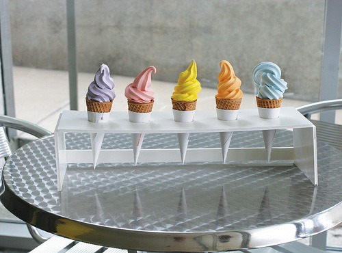 Five ice cream cones holding different flavors sits in a white holder on a metal table.
