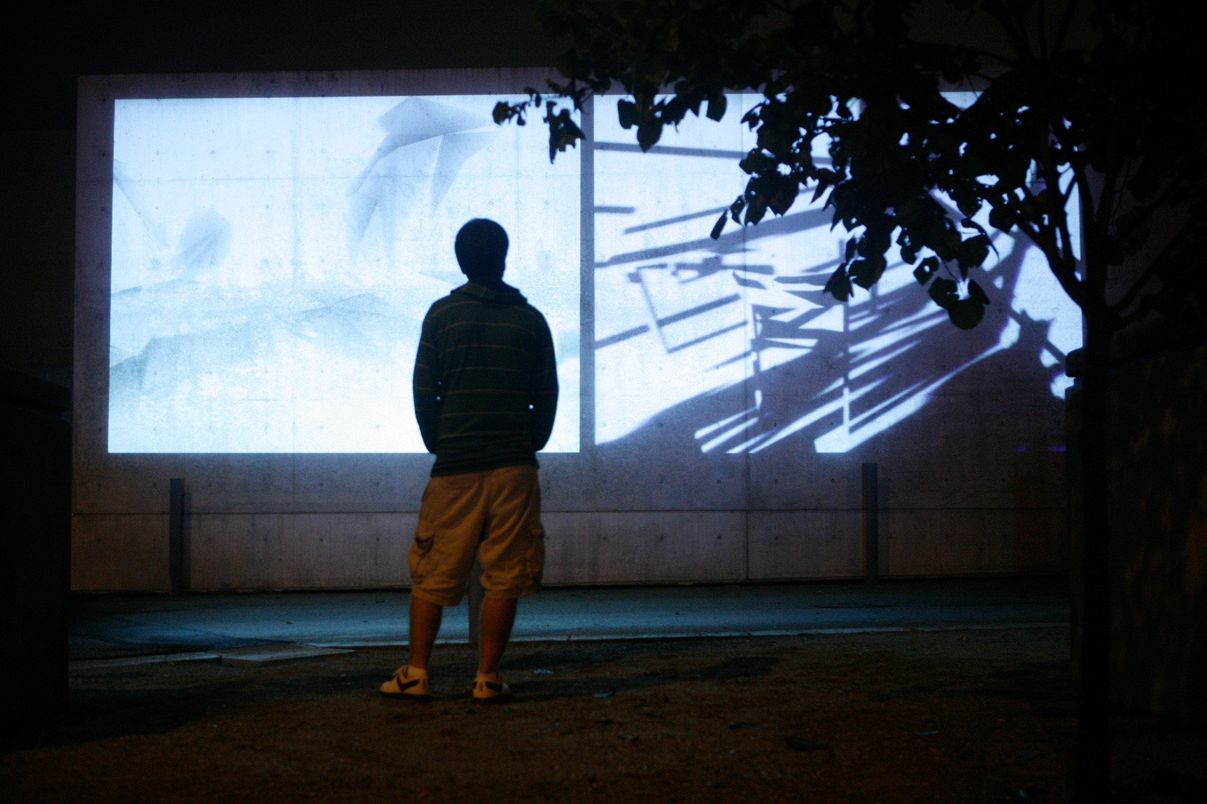 A visitor stands outside before Ann Lislegaard's film "Crystal World" projected on a concrete wall at night.