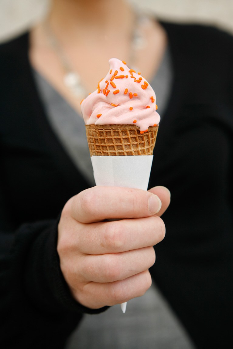 A visitor holds out an ice cream cone filled with orange ice cream.