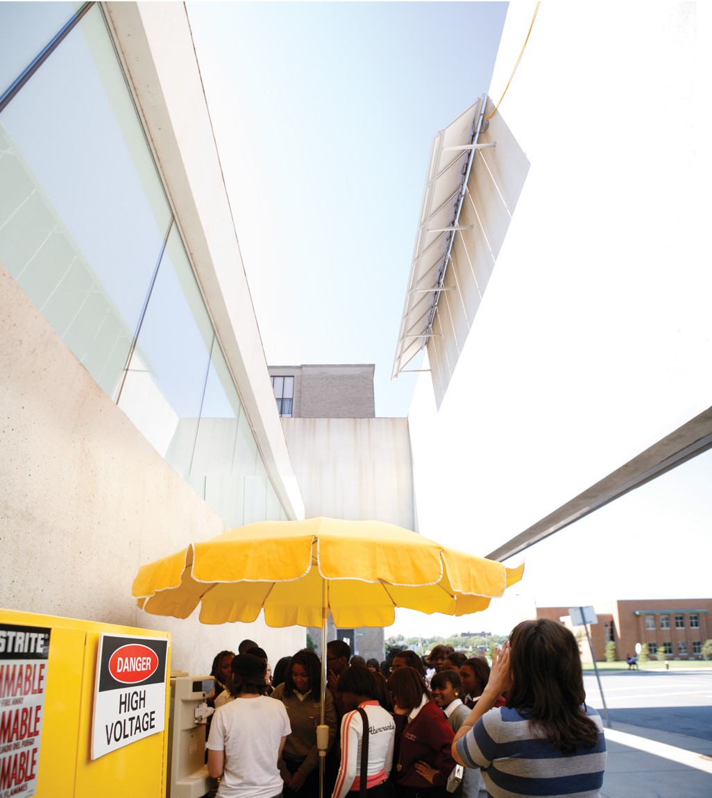 A group gathers around a yellow umbrella in front of CAM.