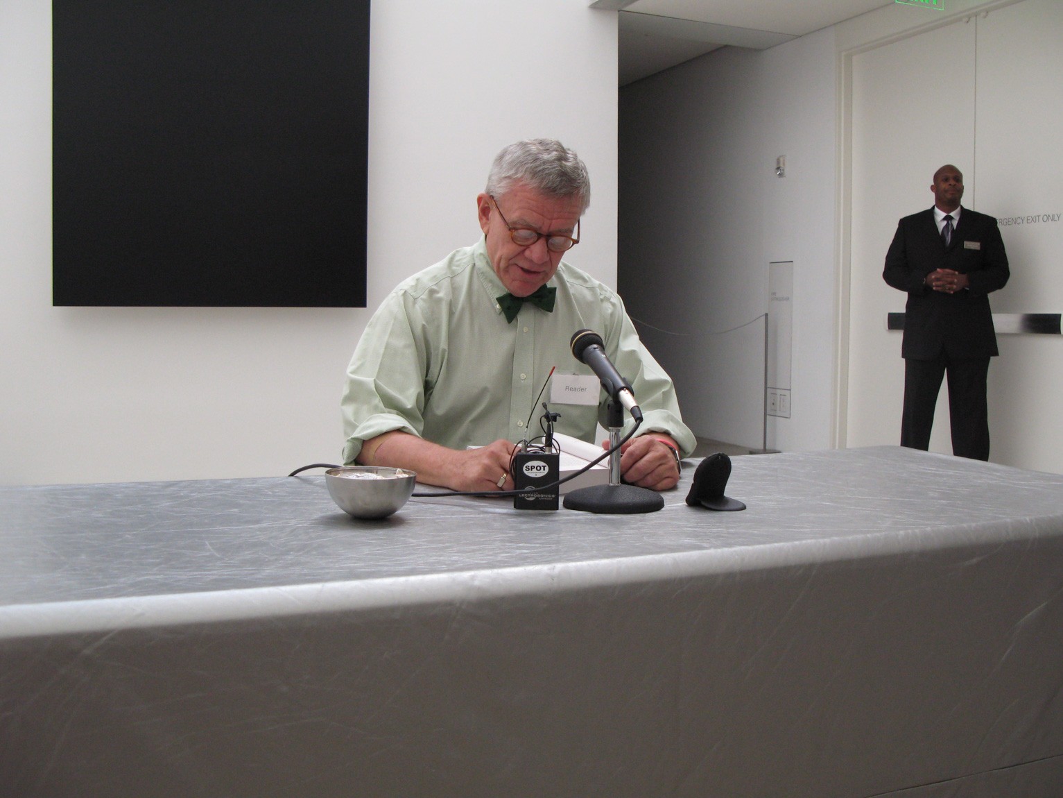 A community member sits at a table in front of Ellsworth Kelly's "Blue Black" and reads from a page into a microphone.
