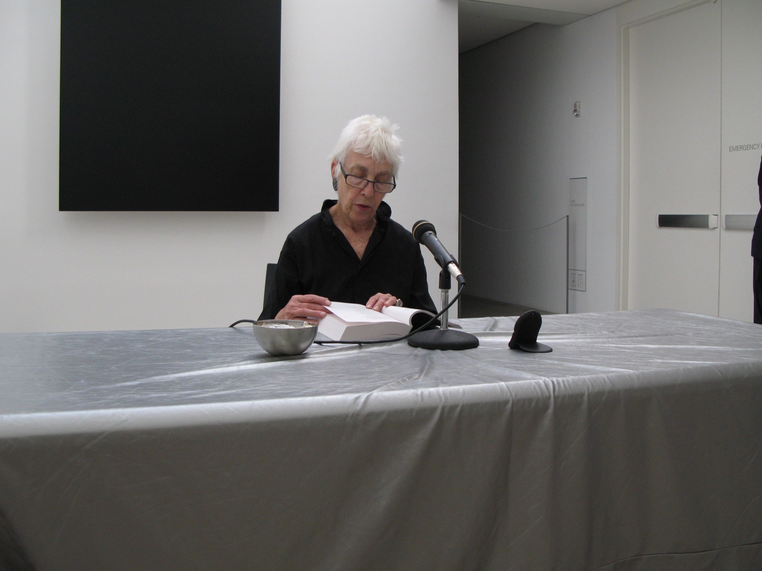 Ms. Pulitzer sits at a table in front of Ellsworth Kelly's "Blue Black" and reads from a page into a microphone.