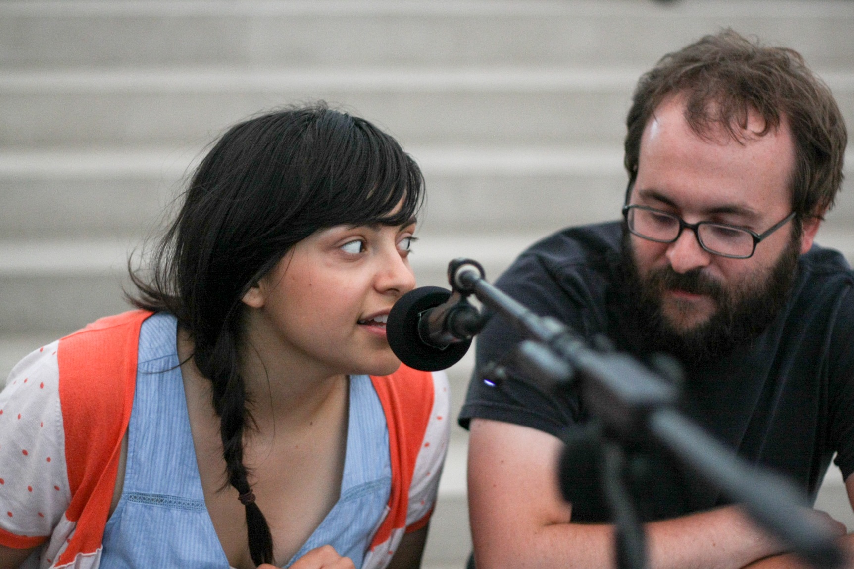 Two people sit on the Main Staircase and one speaks into a microphone.