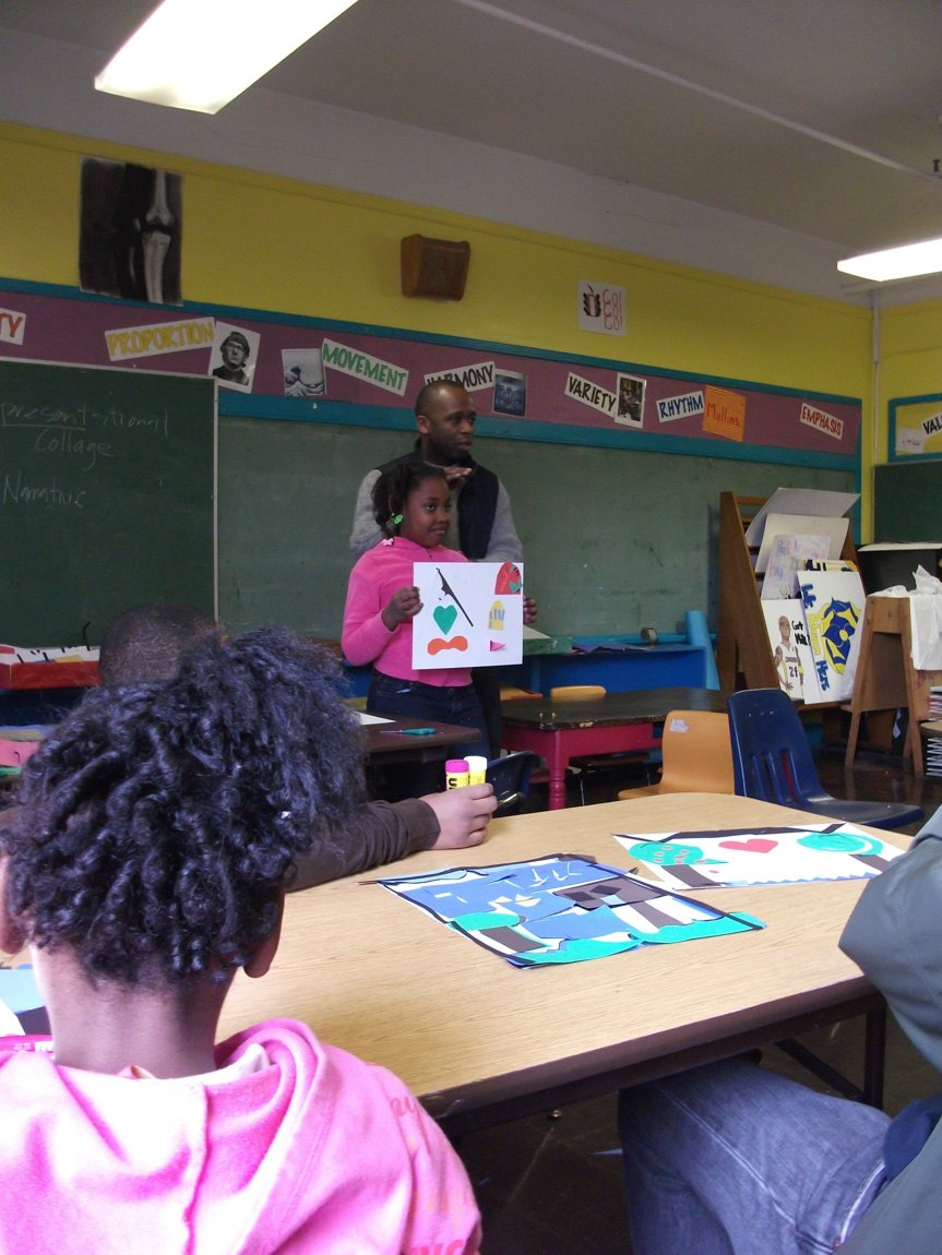 A student and their teacher hold up a small poster for a classroom of students.