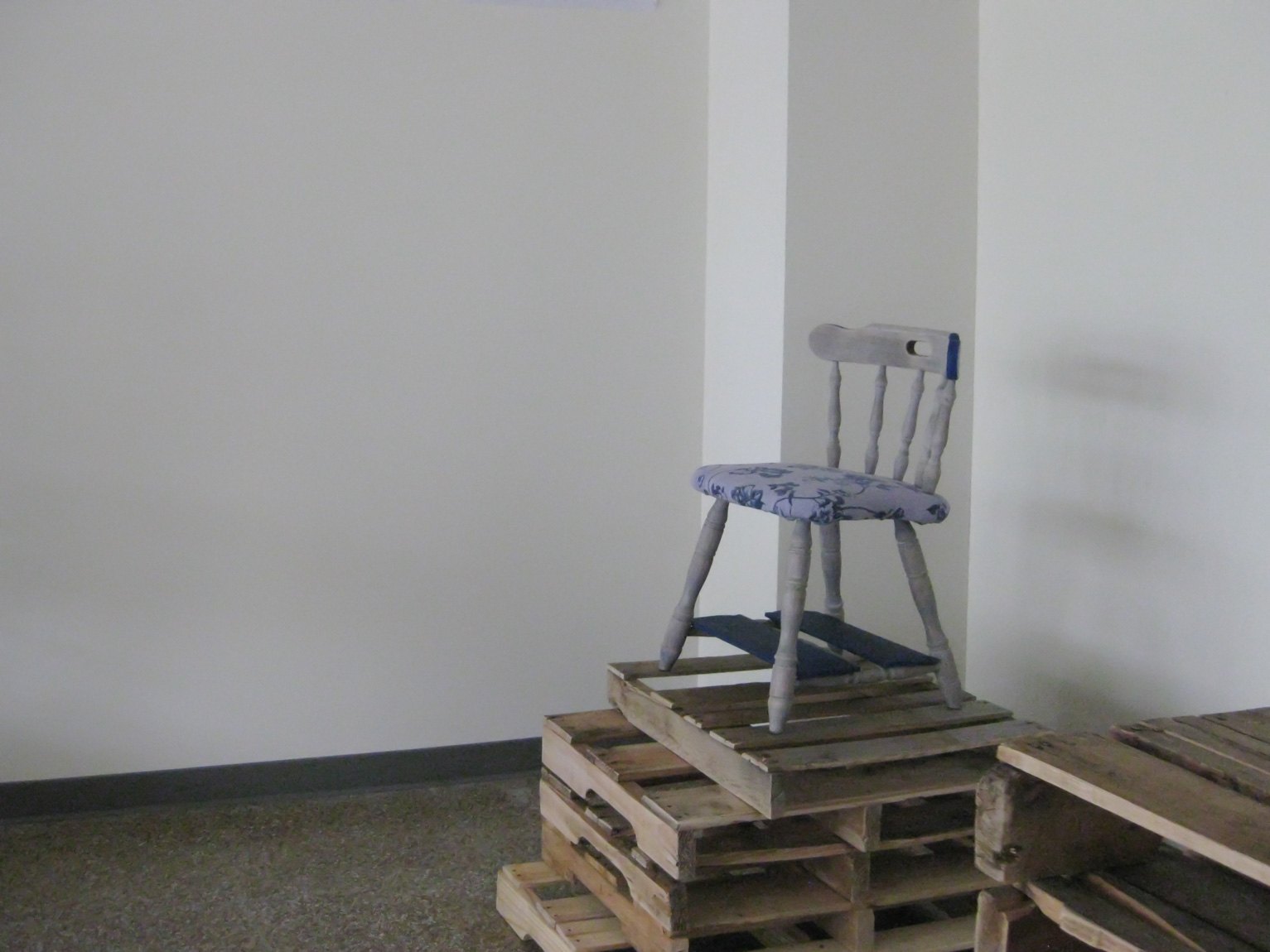 A small white chair sits on a stack of wood pallets.