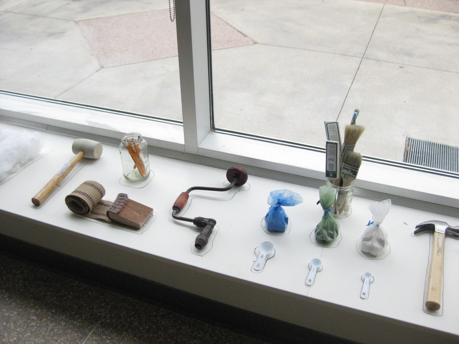 Various tools and utensils arranged on a platform next to a window, their shapes outlined with marker.