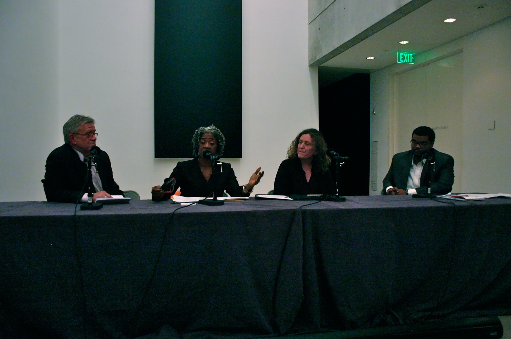 Four panelists sit at a table with microphones in front of Ellsworth Kelly's "Blue Black."