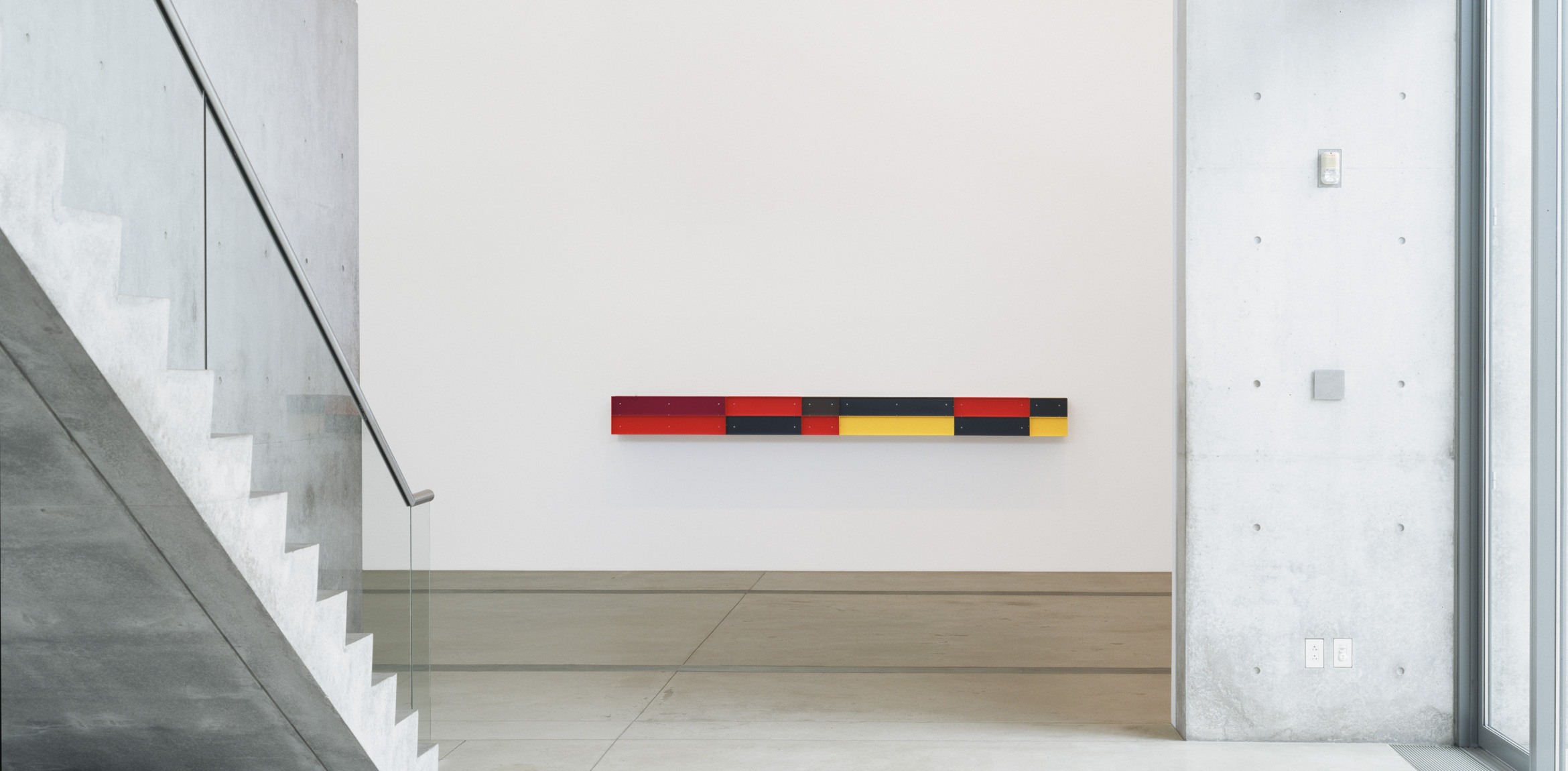 An exhibition shot of an untitled, long, rectangular piece by Judd hangs on the wall in the Main Gallery.