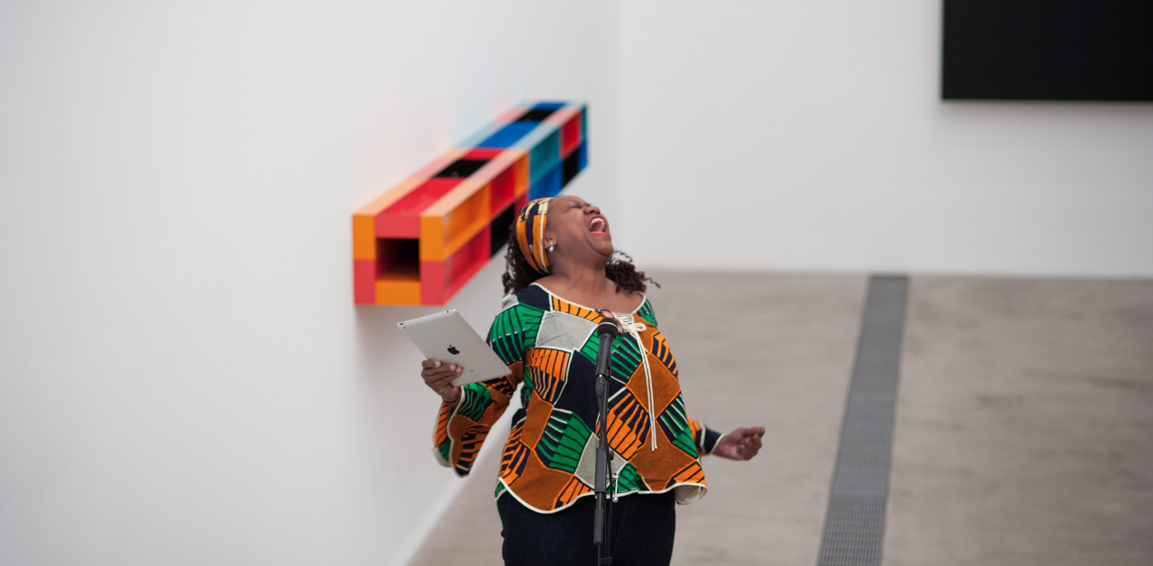 Treasure Shields Redmond gives a passionate performance of her poetry in front of Ellsworth Kelly's "Blue Black," a microphone in front of her and an iPad in her hand.