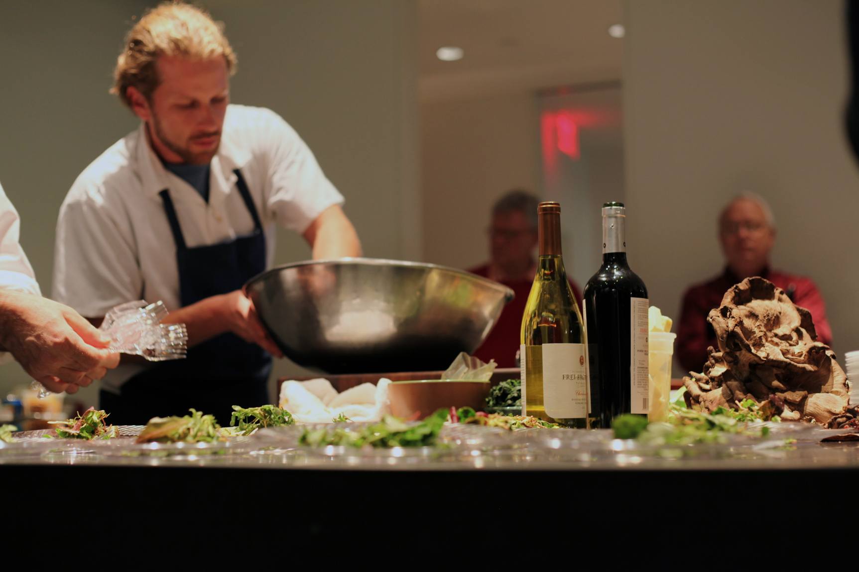 A closeup shot of a chef's table holding salads and wine.