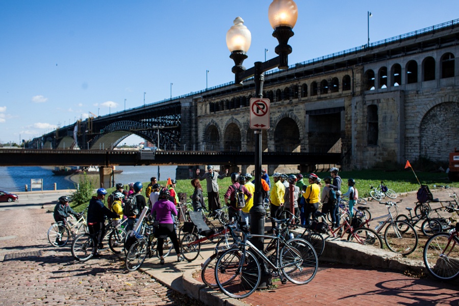 Cycling tour congregates near a bridge on the Mississippi River.