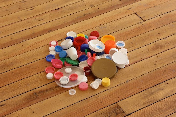 A small pile of bottle caps and jar lids on the light wood floor.