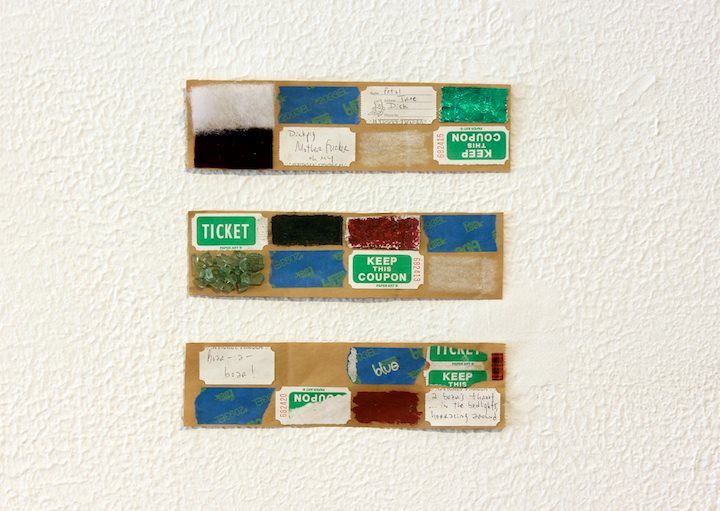 Three long rectangles of cardboard, gridded with coupon tickets, painter's tape, green rocks, and more, arranged in a column on a white wall.