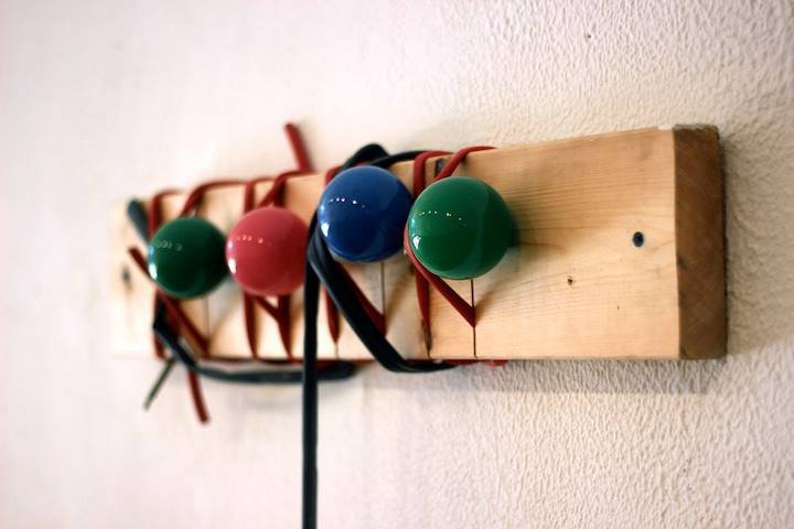 A thin piece of plywood, with different colored balls fastened to it with thin rubber ties, is secured to a wall.