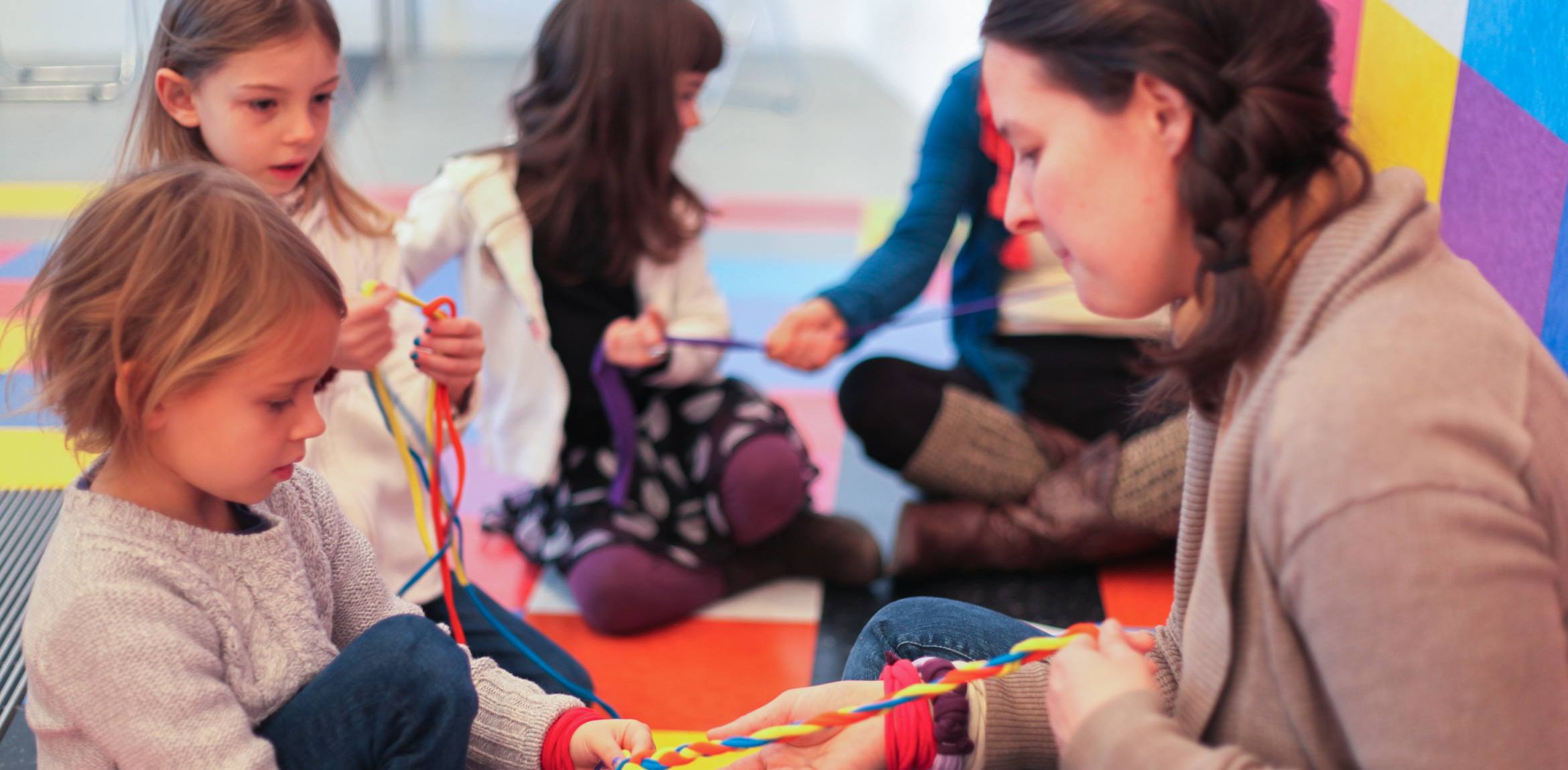 Visitors and their children braid colored ropes together, sitting against David Scanavino's installation "Candy Crush."