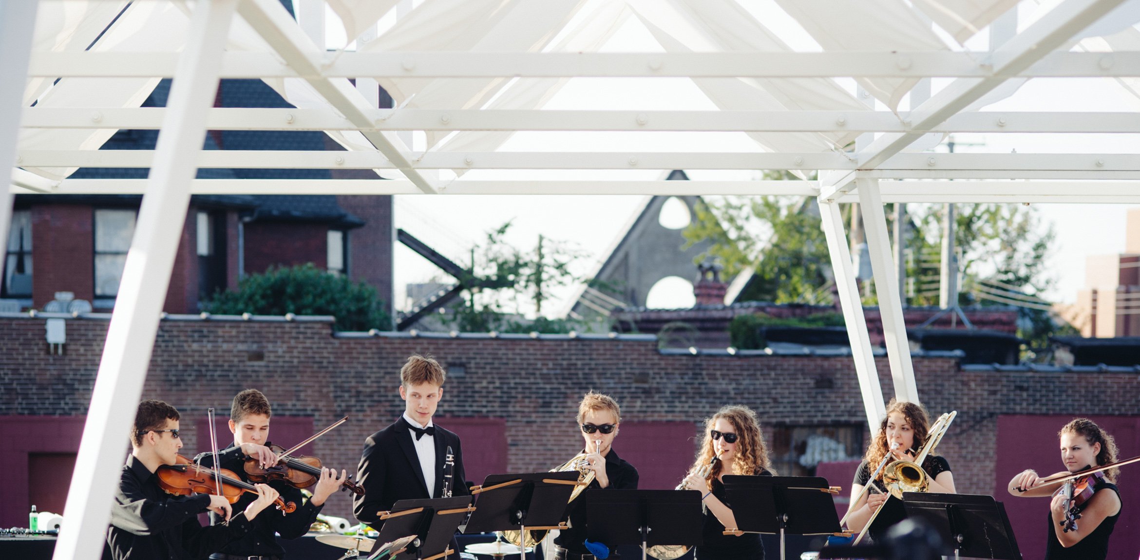 Student musicians perform outdoors under a white geometric canopy installation.