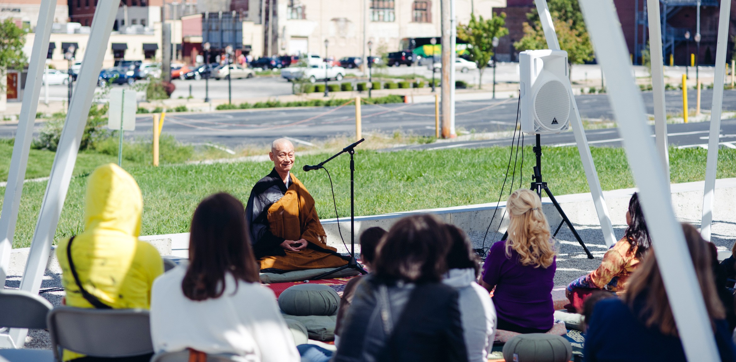 A Buddhist expert leads an audience in outdoor meditation beneath the Lots installation.
