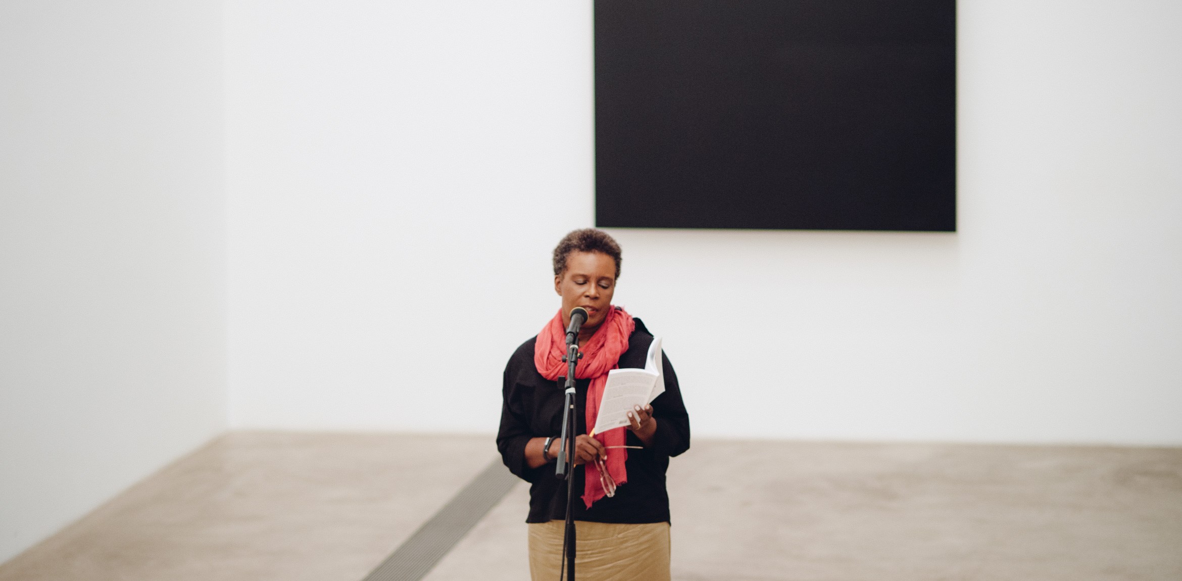 Claudia Rankine reads into a microphone in front of "Blue Black" by Ellsworth Kelly.