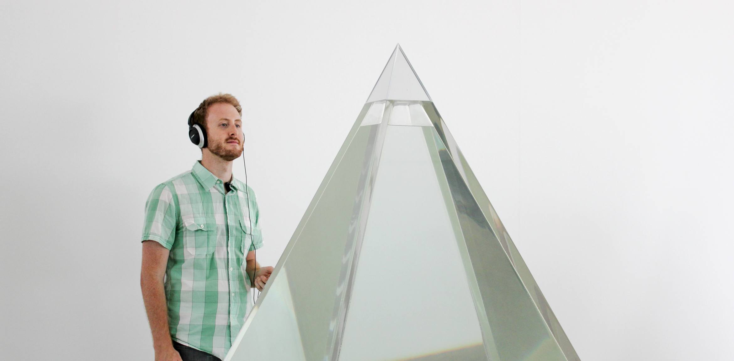 Guest stands behind a large translucent pyramids wearing headphones.