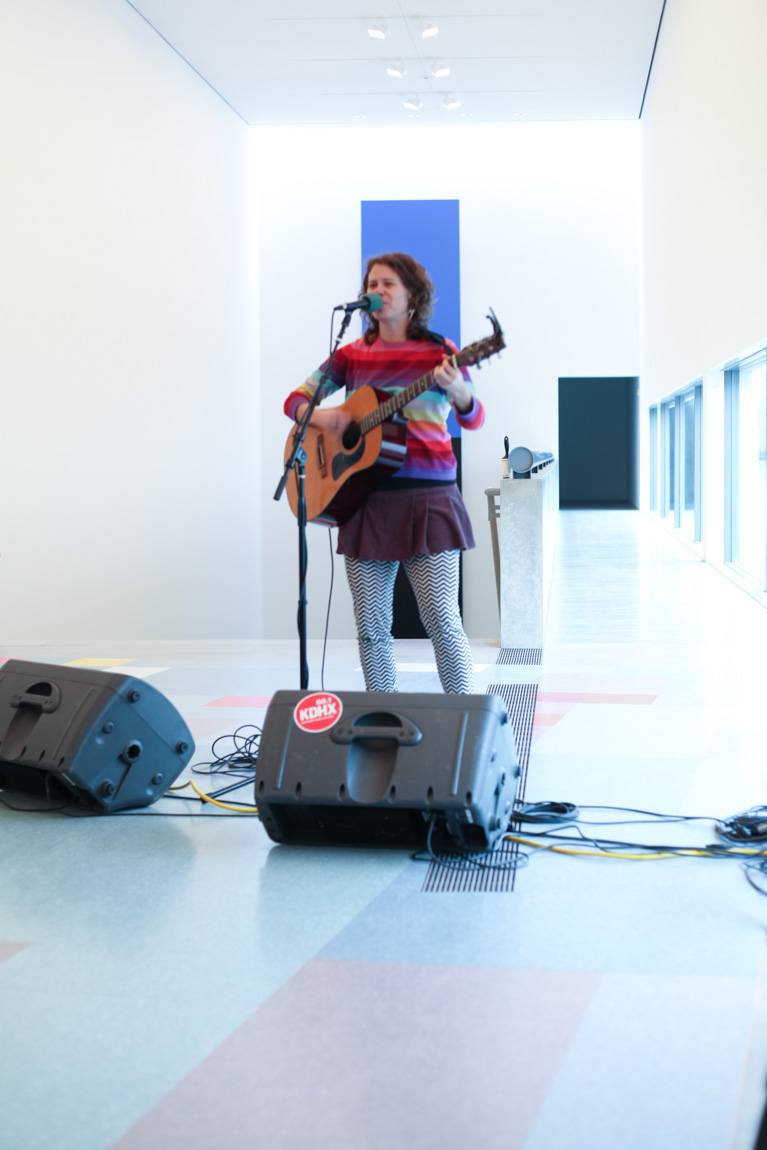 A singer plays a guitar and sings into a microphone in the Main Gallery.