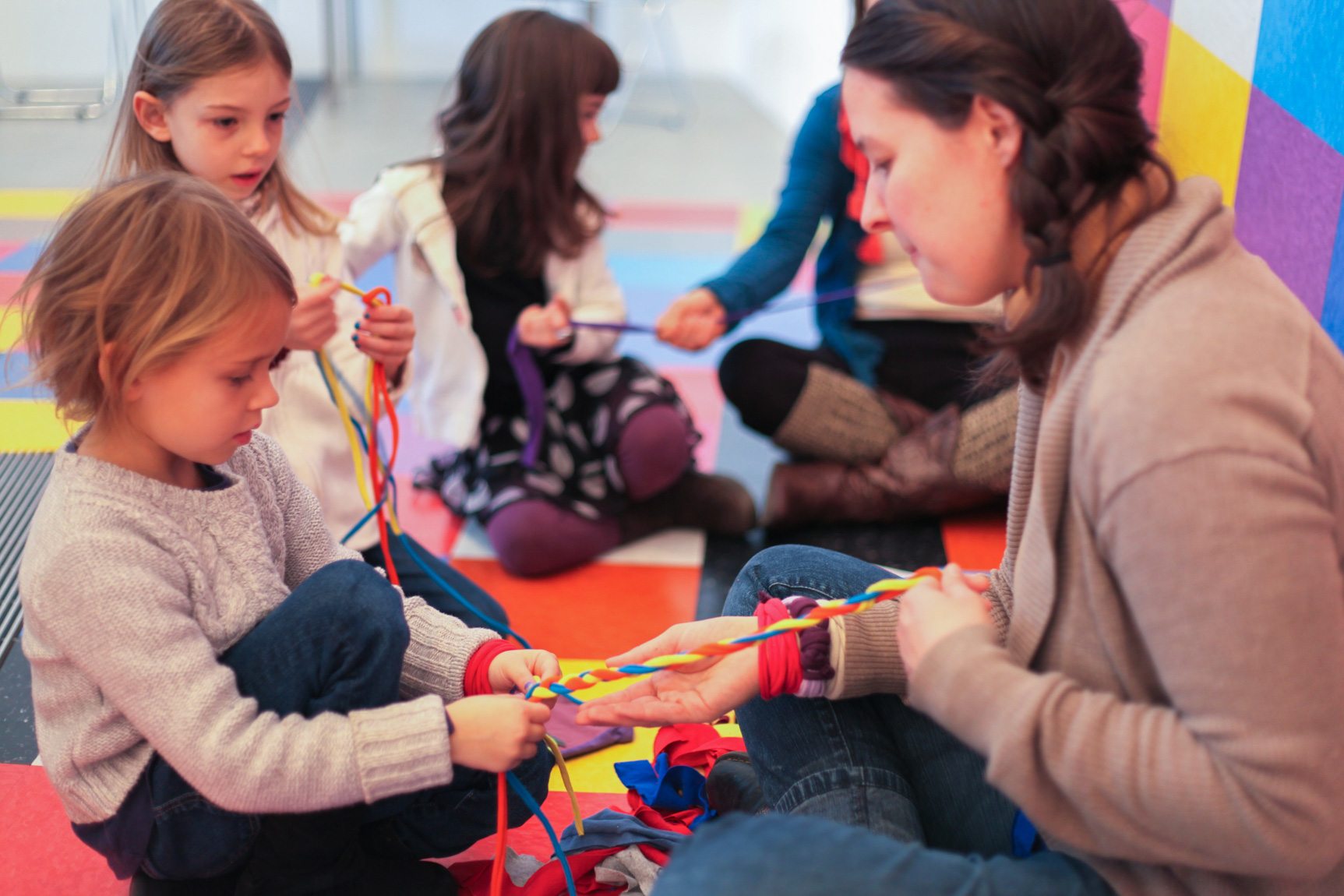 Visitors and their children braid colored ropes together, sitting against David Scanavino's installation "Candy Crush."