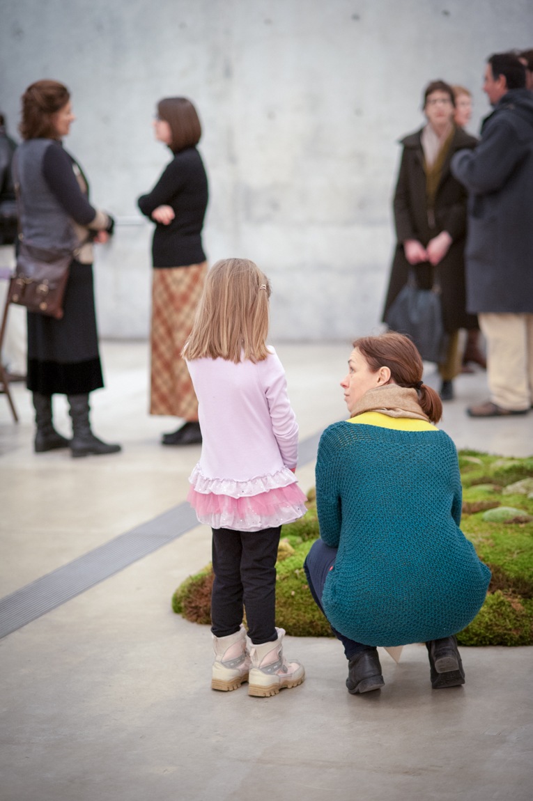 A parent and child observe a mossy installation piece placed on the ground in the Main Gallery.