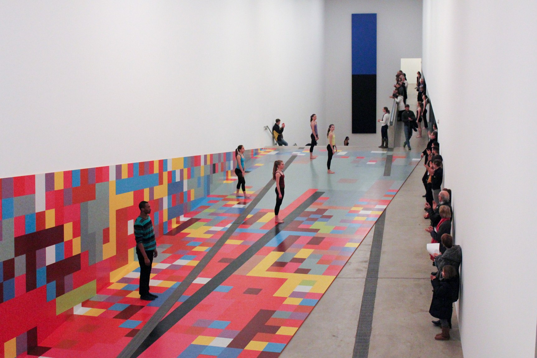 COCA dancers perform with David Scanavino's "Candy Crush" installation. The dancers space out and stand straight up, and an audience applauds them from the opposing wall.