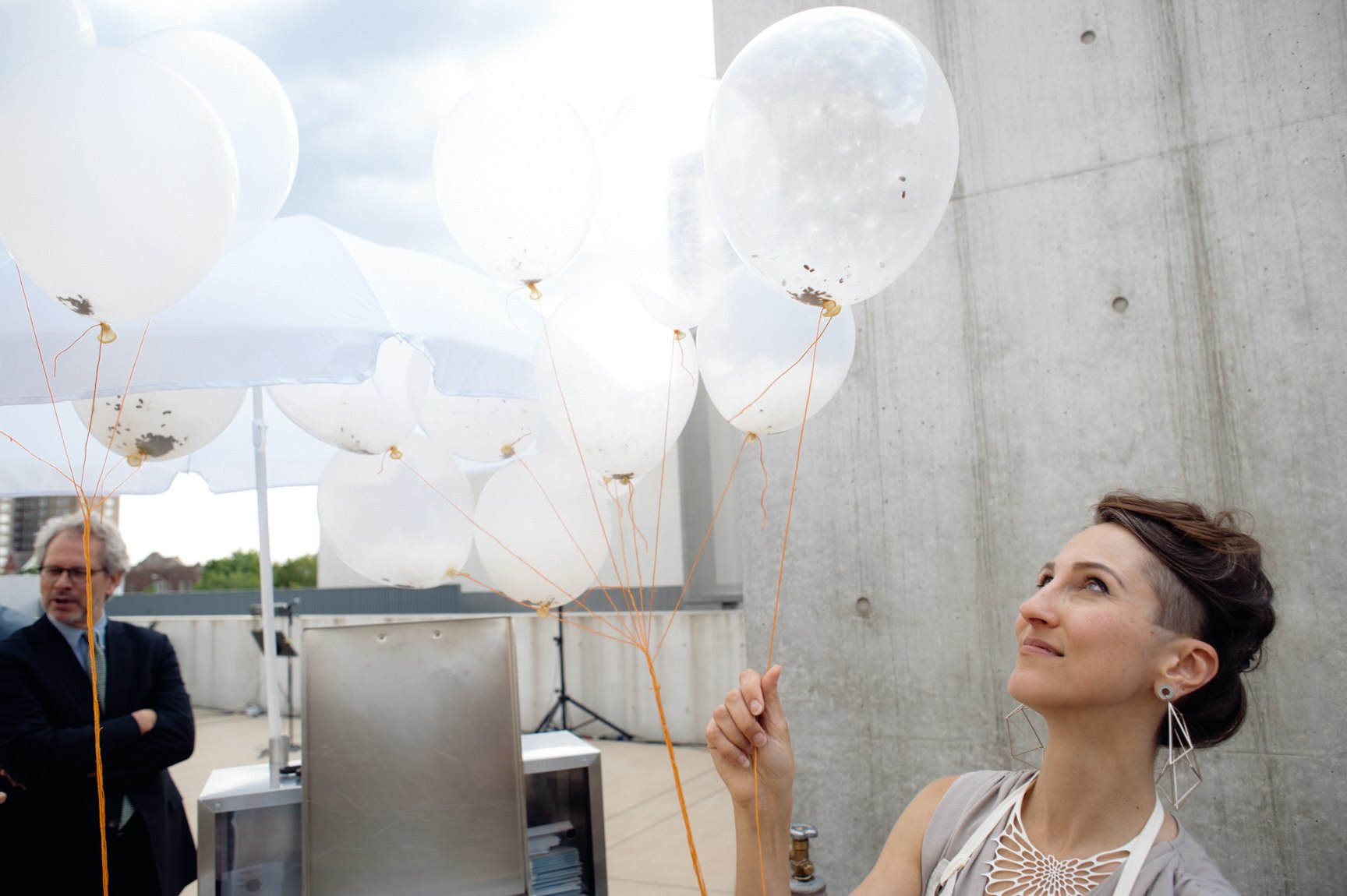 A visitor looks up at their bundle of white balloons.