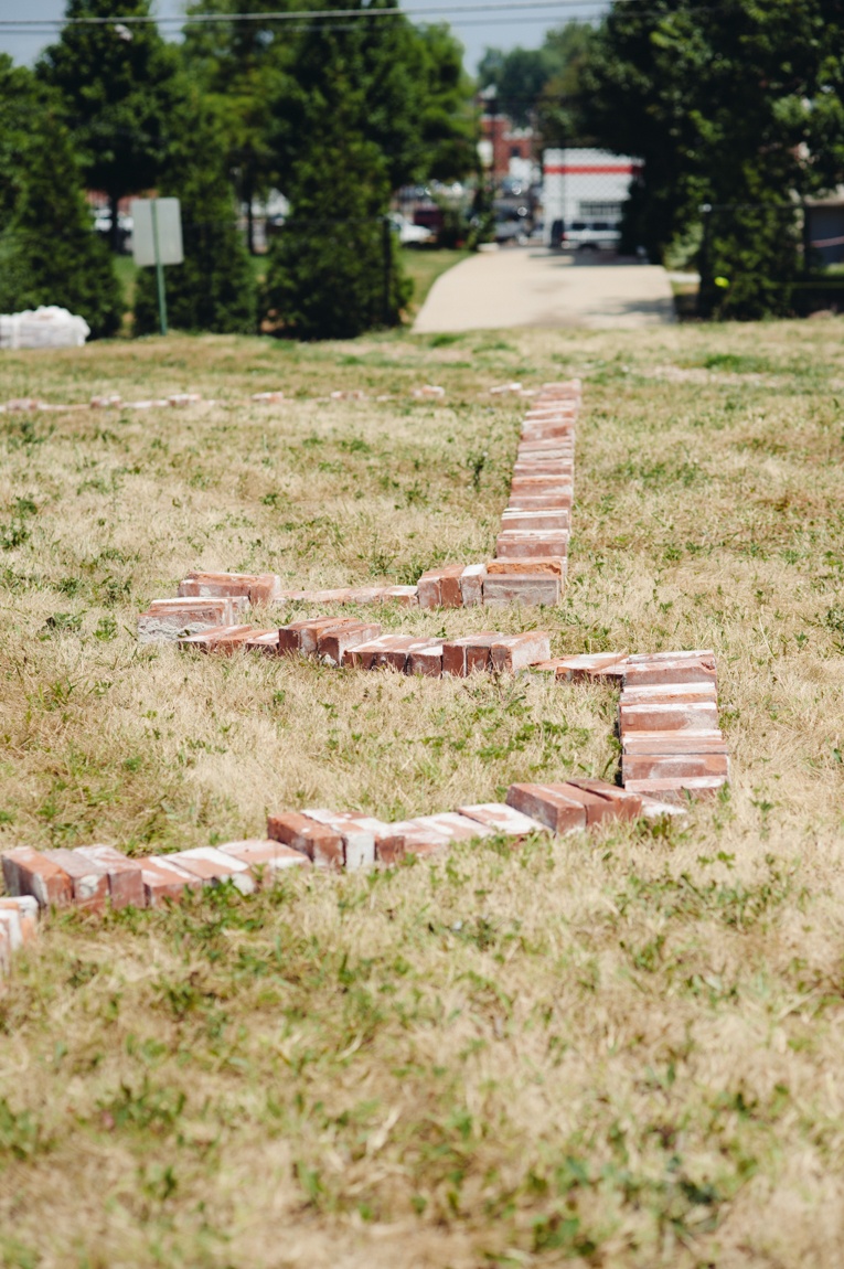 A zigzag line of bricks weaves its way across a grass field.
