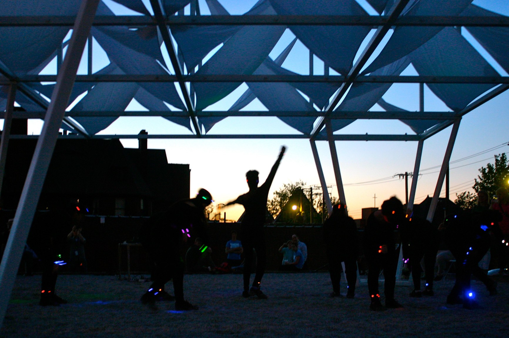 Community members dance in the dark under the Lots installation and colorful designs flash over them.