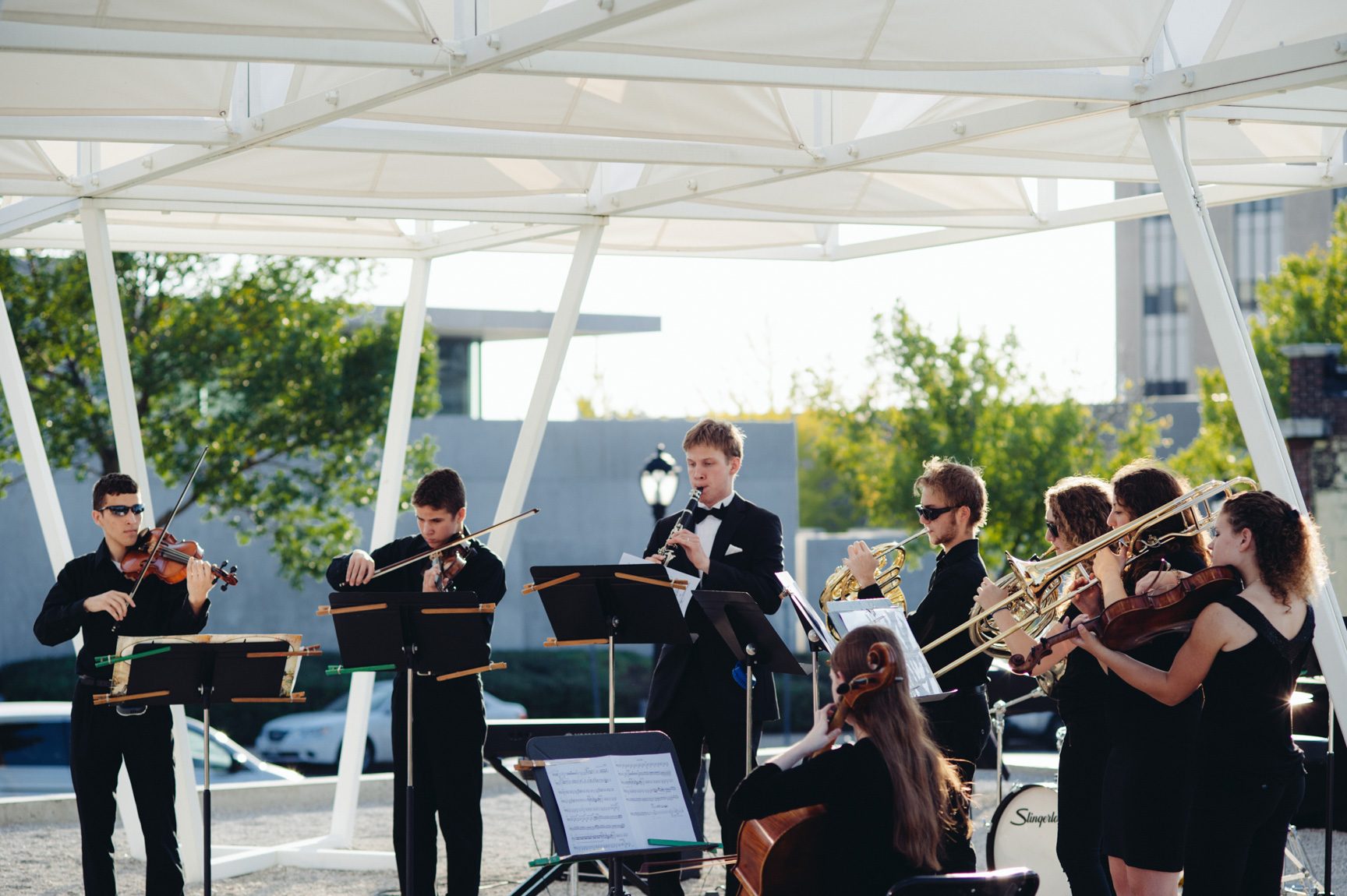 Student musicians perform outdoors under the Lots installation.