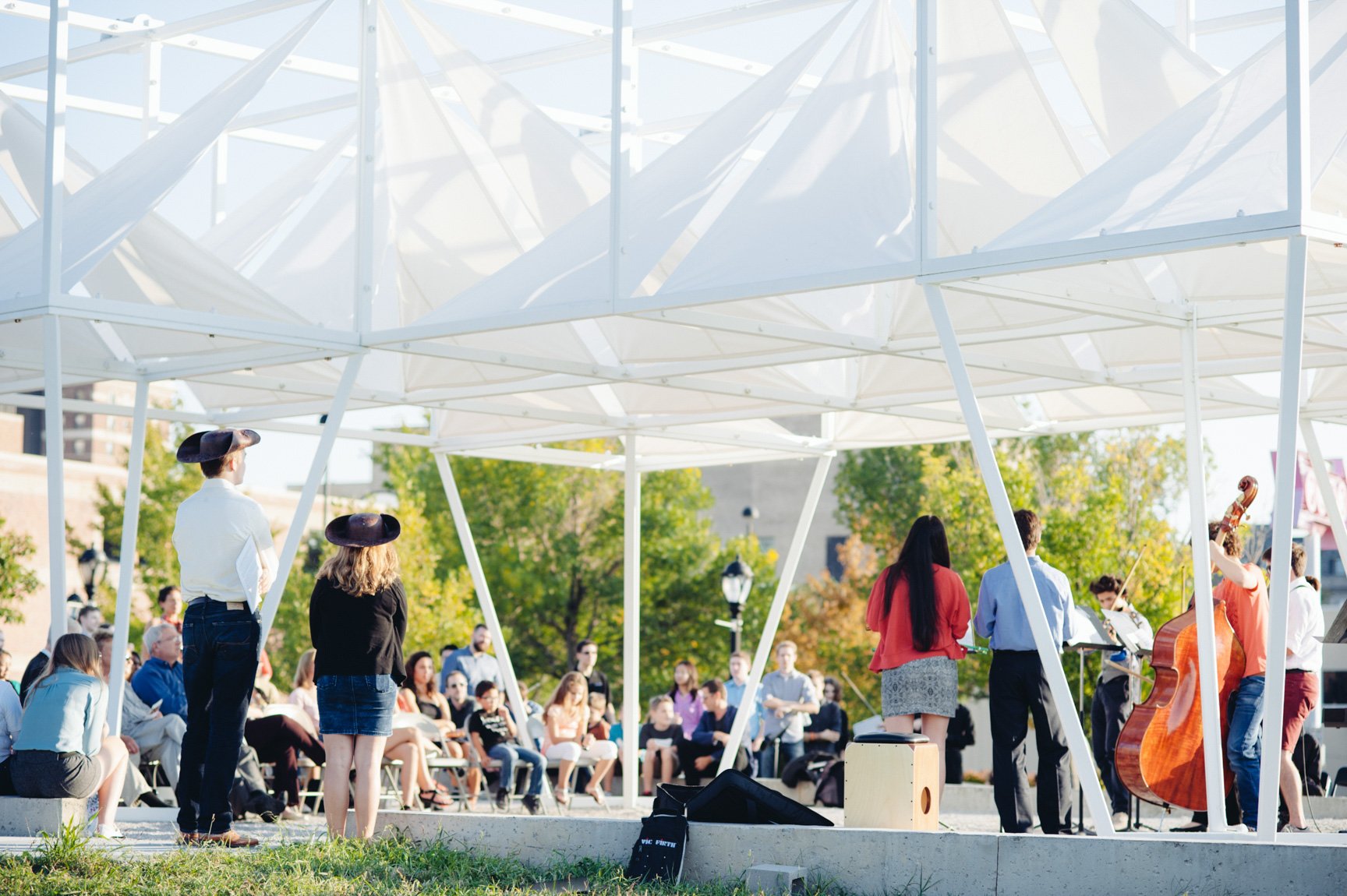 Student musicians perform outdoors under a white geometric installation for an audience.