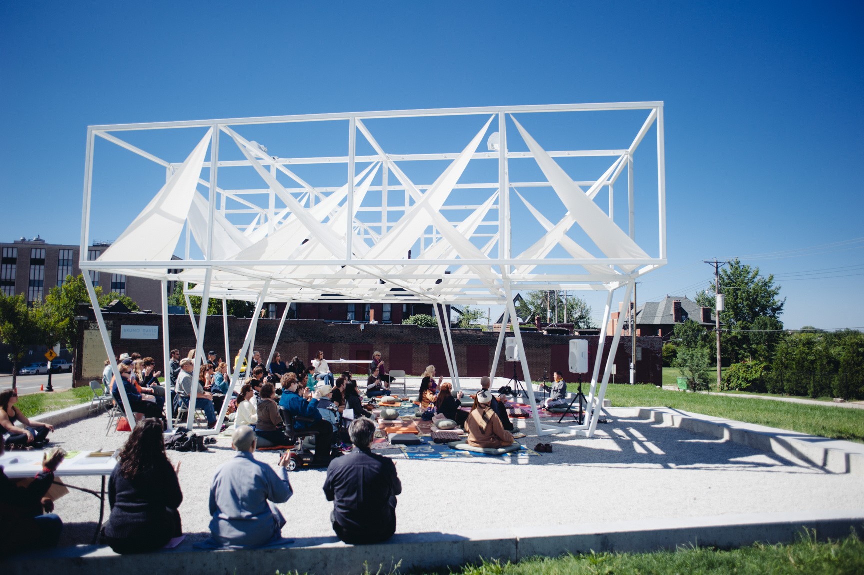 A large audience participates in guided meditation outdoors beneath the Lots installation.