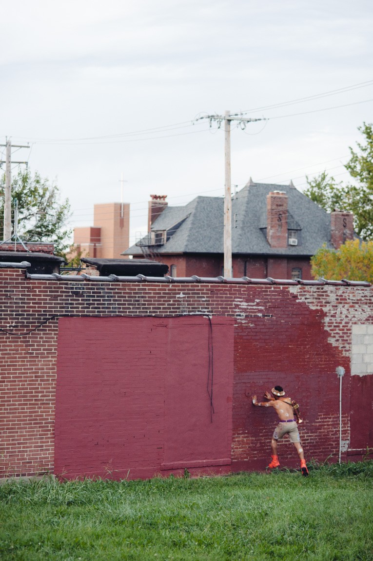 An individual presses their hands against a brick wall in lawn.