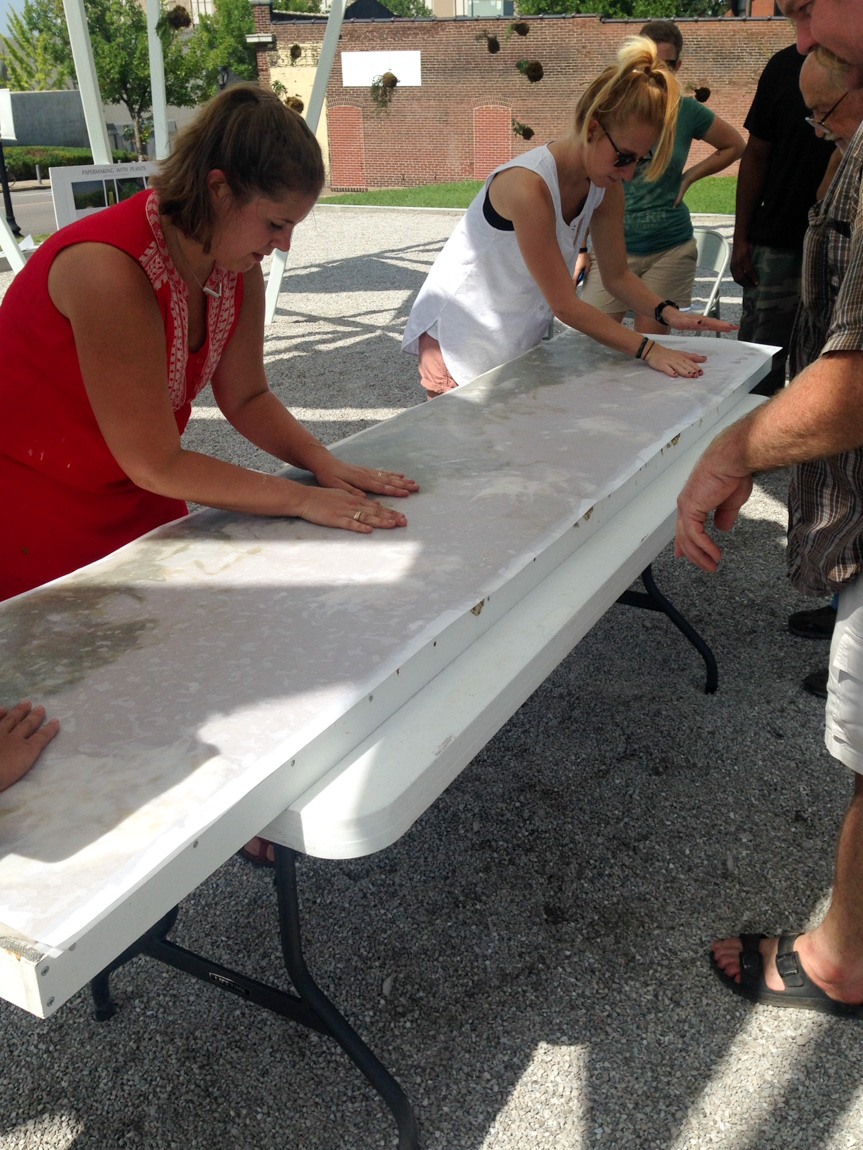 Participants press their hands against a thick white board sitting on a table outside.