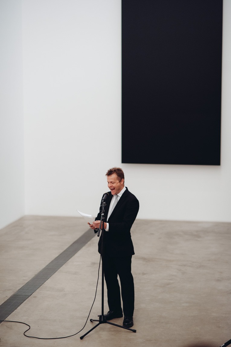 Christian Bök speaks into a microphone on a stand in front of Ellsworth Kelly's "Blue Black."