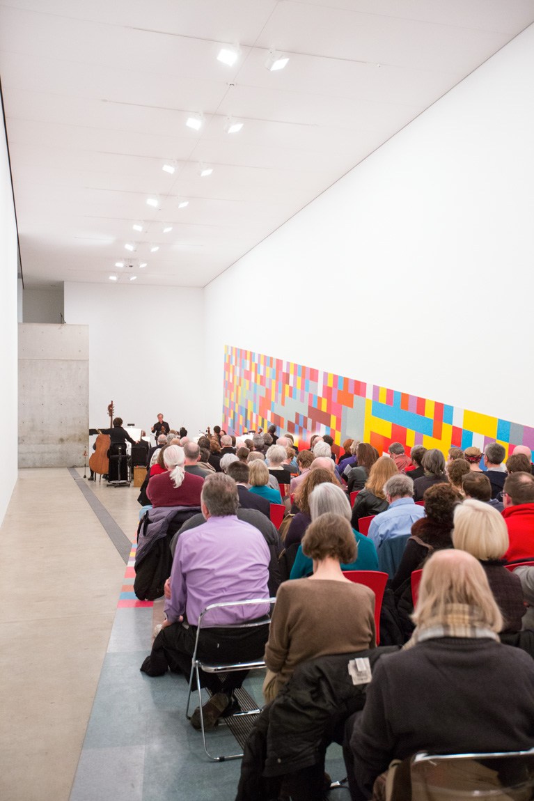 A large audience sits in rows in the Main Gallery during the concert, framed by David Scanavino's installation "Candy Crush."
