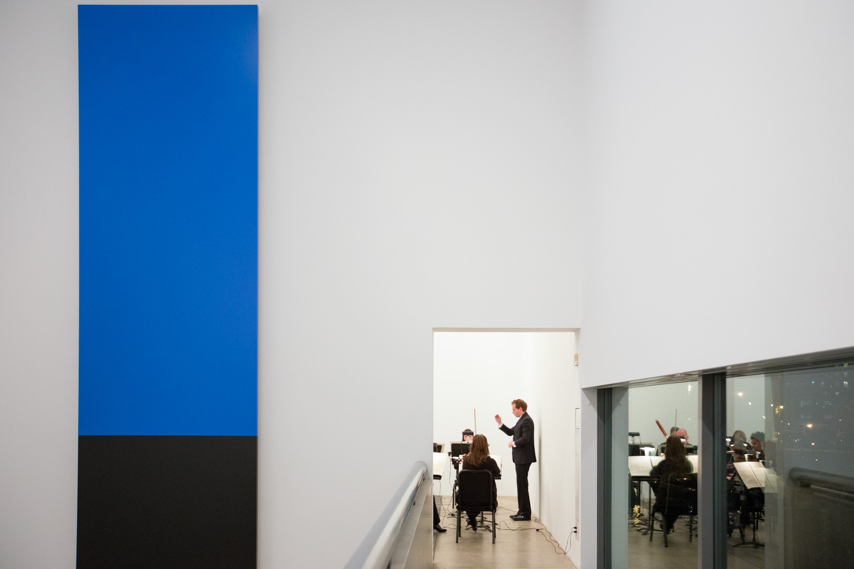 A view of the conductor and ensemble performing in the Cube Gallery, with Kelly's "Blue Black" on the left.
