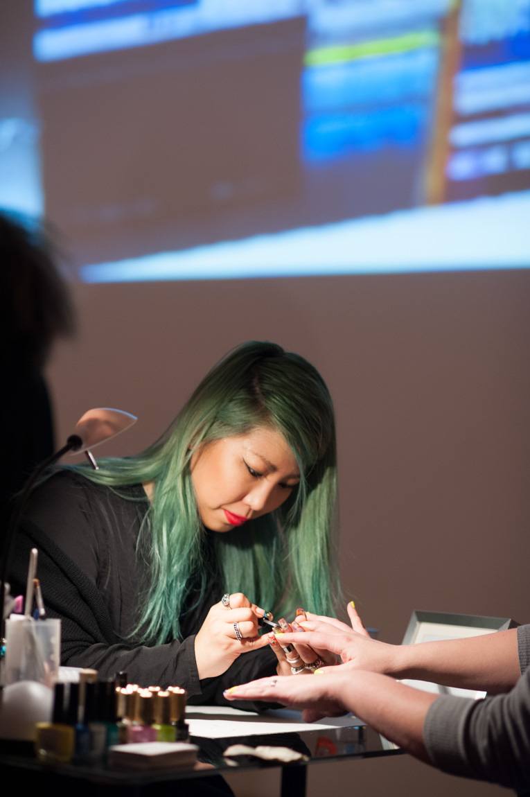 A nail artist applies polish to a visitor's fingers.