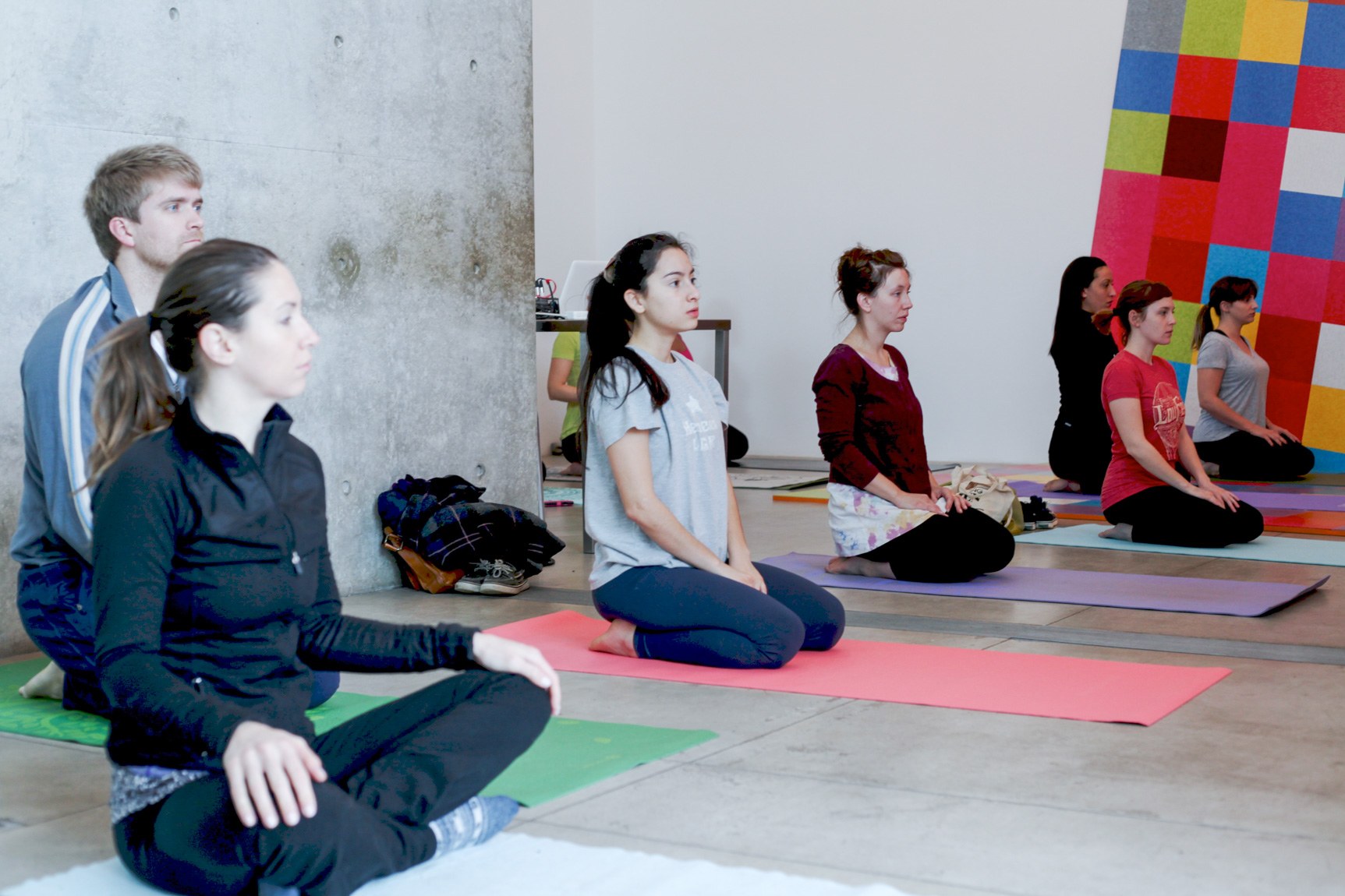 Yoga participants sit on yoga mats in the Main Gallery facing the instructor.